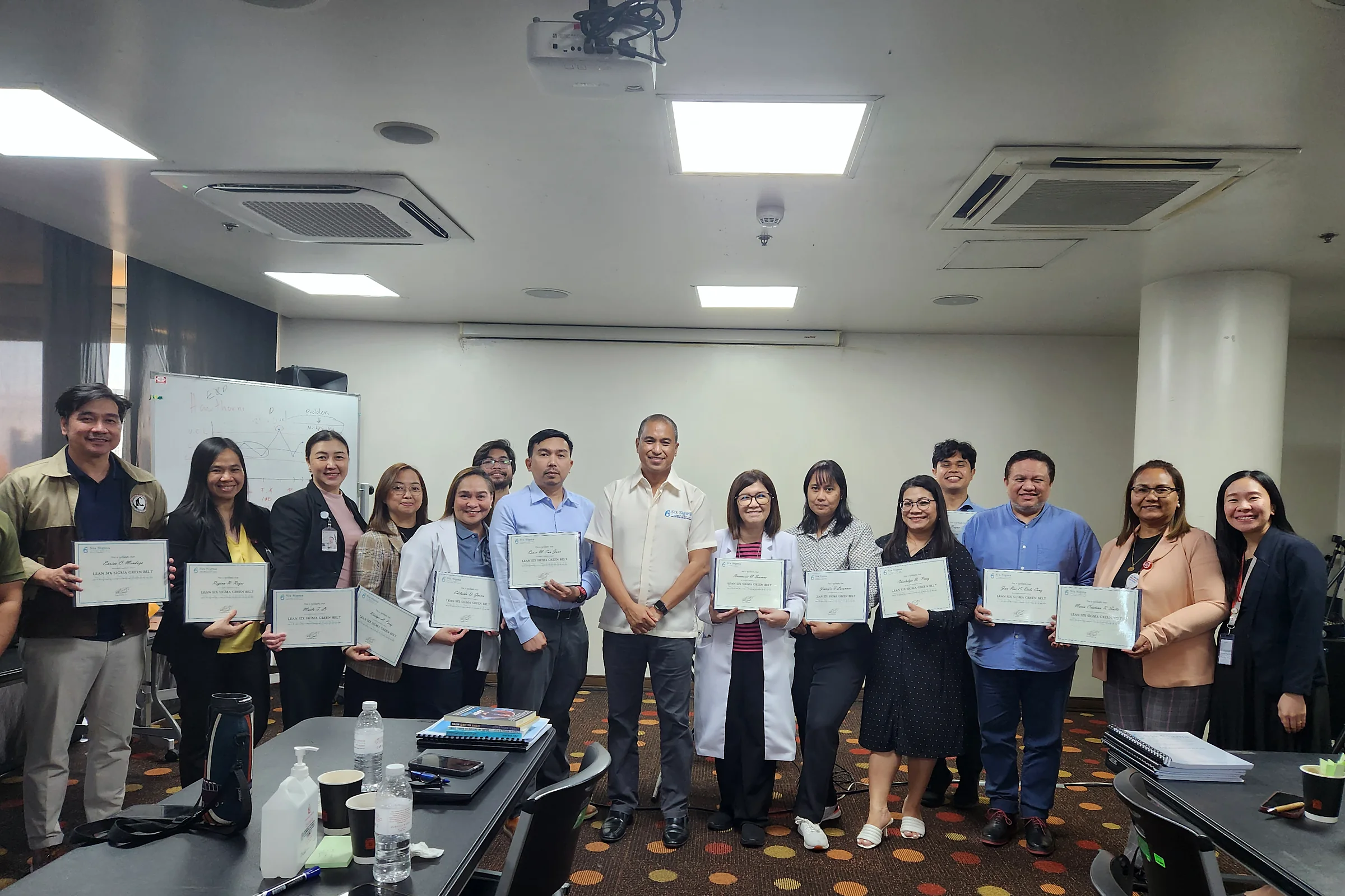 A group of about twenty participants standing in a training room, each holding up a certificate
